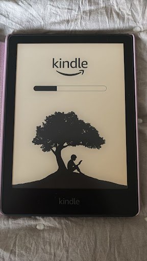 Kindle Paperwhite preto metálico com capa protetora roxa e tela de 7 polegadas, exibindo imagem da tela inicial.